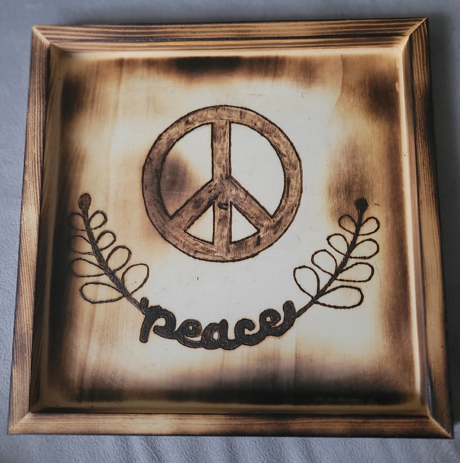 Gerahmte Brandmalerei mit Peace-Zeichen und Schriftzug auf hellem Holz